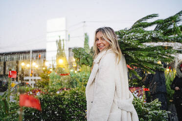 Happy woman carrying Christmas tree at market - MDOF01478