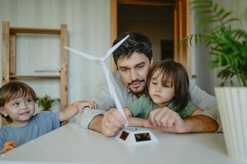 Father and sons examining wind turbine model at home - ANAF02099