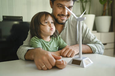 Boy blowing on wind turbine model at home - ANAF02100