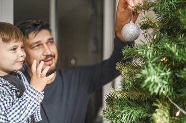 Vater hängt Ornament an den Weihnachtsbaum zu Hause - ANAF02110