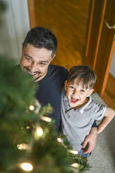 Lächelnder Vater und Sohn betrachten einen geschmückten Weihnachtsbaum - ANAF02115