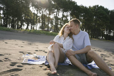 Romantisches Paar sitzt am Strand an einem sonnigen Tag - YBF00196