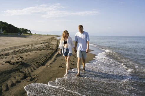 Couple walking barefoot at beach on sunny day - YBF00197