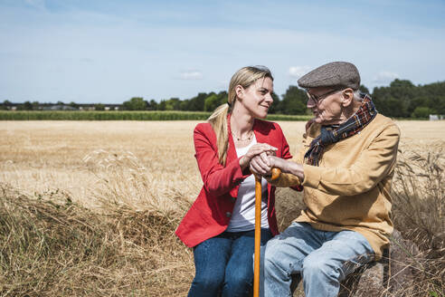 Smiling woman talking with senior man in field on sunny day - UUF30185