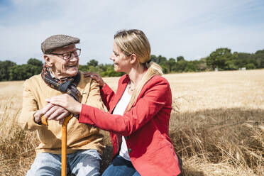 Cheerful elderly man talking with woman in field on sunny day - UUF30189