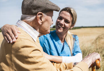 Smiling nurse putting arm around elderly man on sunny day - UUF30193