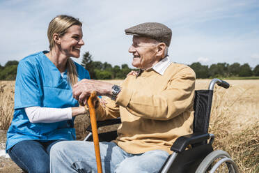 Glücklicher älterer Mann im Rollstuhl sitzend und im Gespräch mit einer Krankenschwester - UUF30199