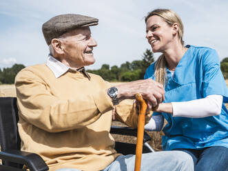 Glückliche Pflegekraft im Gespräch mit einem älteren Mann im Rollstuhl - UUF30200