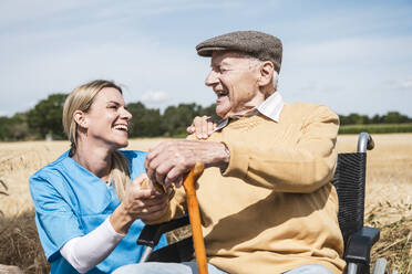 Krankenschwester und älterer Mann mit Behinderung lachen an einem sonnigen Tag - UUF30201