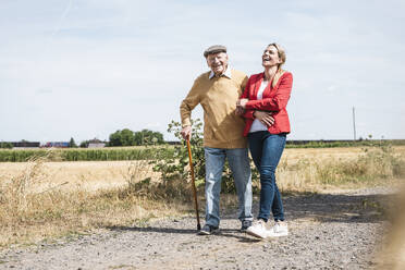 Glücklicher älterer Mann, der eine Frau unterstützt und an einem sonnigen Tag spazieren geht - UUF30202