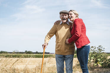 Cheerful woman embracing elderly man standing by field - UUF30203