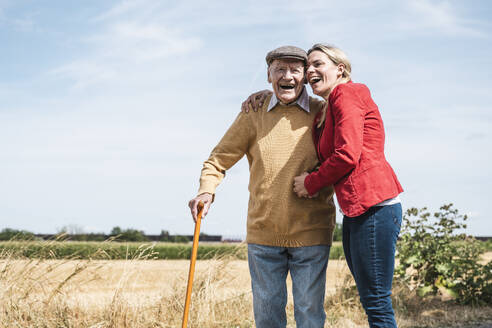 Cheerful woman embracing elderly man standing by field - UUF30203
