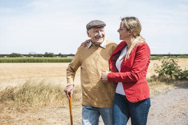Lächelnder älterer Mann, der mit einer Frau durch ein Feld an einem sonnigen Tag spaziert - UUF30205