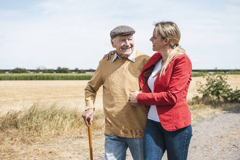 Smiling senior man walking with woman by field on sunny day - UUF30205