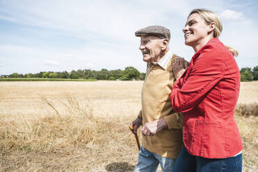 Lächelnde Frau geht mit älterem Mann an einem sonnigen Tag spazieren - UUF30207