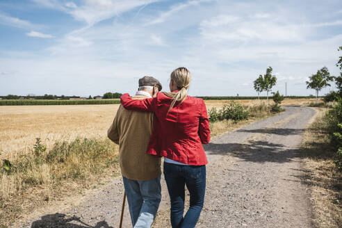 Woman with arm around senior man walking by field - UUF30208