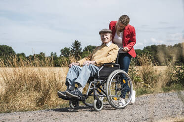 Woman pushing senior man with disability sitting in wheelchair - UUF30210