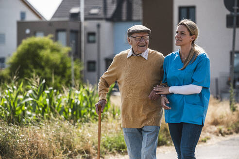 Glücklicher älterer Mann geht mit Krankenschwester an einem sonnigen Tag spazieren - UUF30222
