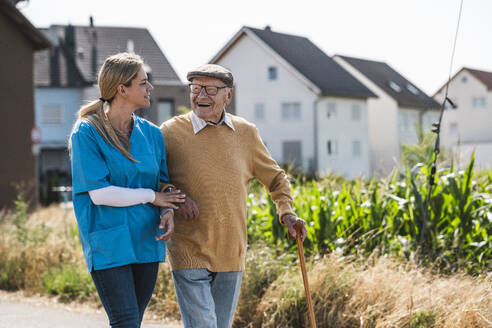 Elderly man and healthcare worker walking on sunny day - UUF30223