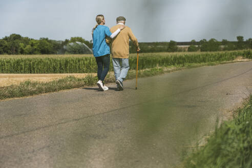 Healthcare worker walking with senior man on road at sunny day - UUF30225
