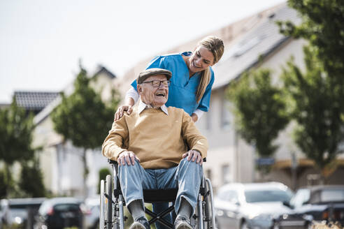 Happy elderly man sitting in wheelchair and talking with nurse - UUF30231