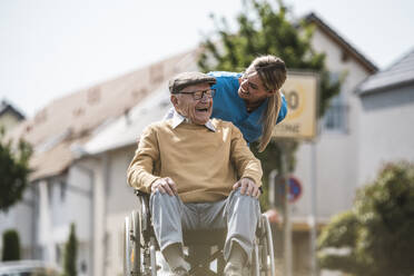 Gut gelaunte Krankenschwester im Gespräch mit einem älteren Mann im Rollstuhl - UUF30232