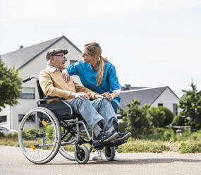 Mitarbeiter des Gesundheitswesens im Gespräch mit einem älteren Mann, der im Rollstuhl sitzt - UUF30236