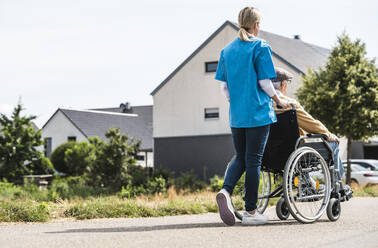 Krankenschwester schiebt älteren Mann im Rollstuhl sitzend - UUF30237