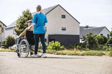 Healthcare worker pushing elderly man sitting in wheelchair - UUF30238