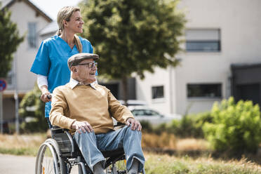 Lächelnde Krankenschwester schiebt älteren Mann im Rollstuhl sitzend - UUF30239