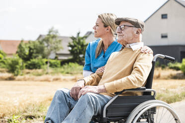 Thoughtful nurse by senior man sitting in wheelchair - UUF30241