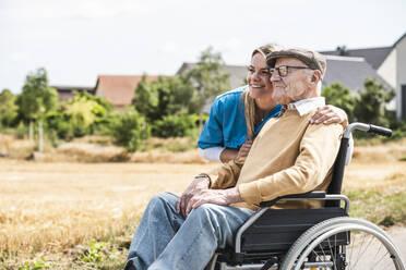 Smiling nurse embracing senior man sitting in wheelchair - UUF30243