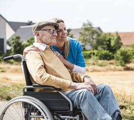 Lächelnde Krankenschwester umarmt älteren Mann im Rollstuhl sitzend - UUF30244