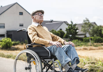 Elderly man sitting in wheelchair in front of houses - UUF30245
