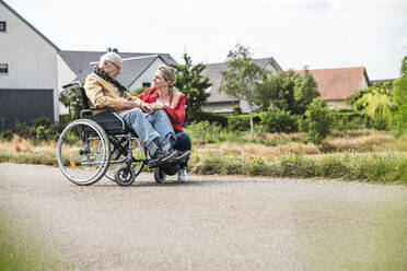 Woman talking with senior man sitting in wheelchair on road - UUF30249