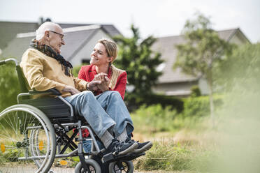 Smiling woman holding hand of senior man sitting in wheelchair - UUF30251