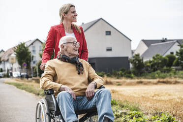 Glückliche Frau mit älterem Mann im Rollstuhl auf der Straße sitzend - UUF30255