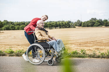 Fröhlicher älterer Mann im Rollstuhl sitzend mit einer dahinter stehenden Frau - UUF30257