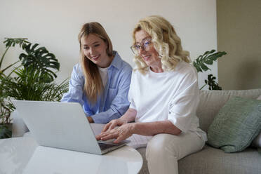 Lächelnde Frau mit Mutter, die zu Hause einen Laptop benutzt - AAZF00975