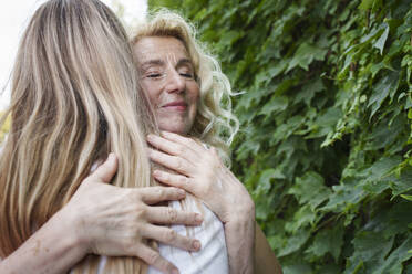 Smiling senior woman hugging daughter near plants - AAZF00995