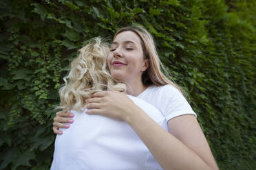 Smiling blond woman hugging mother in front of plants - AAZF01000