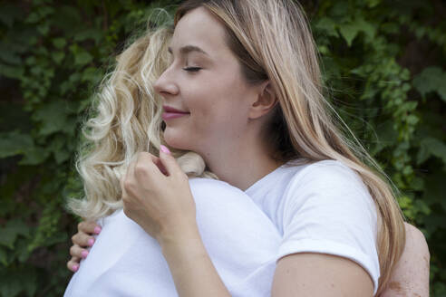 Smiling young woman hugging mother in front of plants - AAZF01001