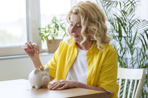 Lächelnde ältere Frau spart Geld im Sparschwein - AAZF01023
