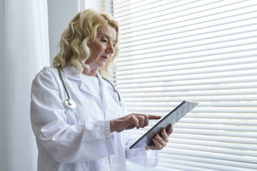 Oberarzt mit Tablet-PC am Fenster in der Klinik - AAZF01029