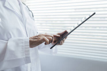 Hände eines Oberarztes, der einen Tablet-PC am Fenster benutzt - AAZF01030