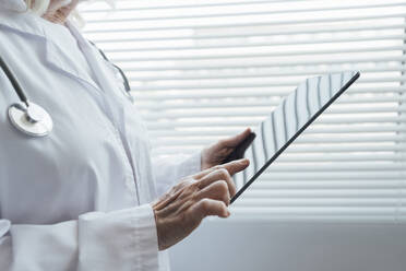 Hände eines Oberarztes, der vor einem Fenster einen Tablet-PC benutzt - AAZF01031