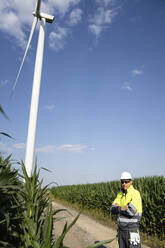 Engineer with arms crossed standing in front of plants on sunny day - EKGF00485