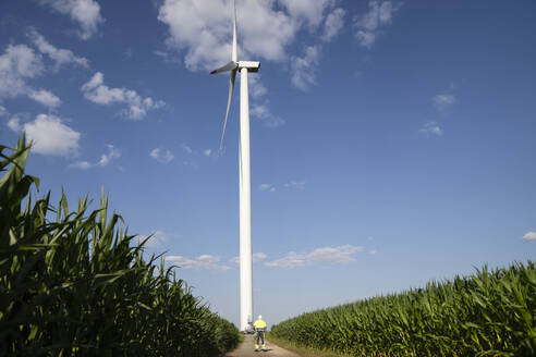 Ingenieur vor einer Windkraftanlage bei bewölktem Himmel - EKGF00486