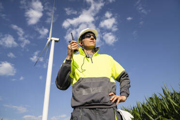 Engineer with walkie-talkie standing in field under sky with clouds - EKGF00488