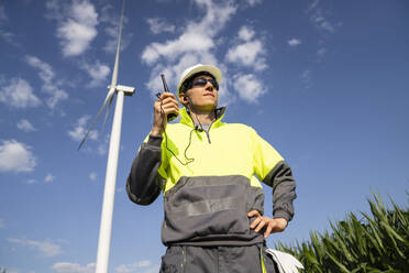 Ingenieur mit Walkie-Talkie in einem Feld unter einem Wolkenhimmel stehend - EKGF00488